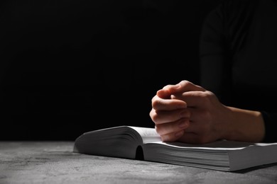 Photo of Religion. Christian woman praying over Bible at table against black background, closeup. Space for text