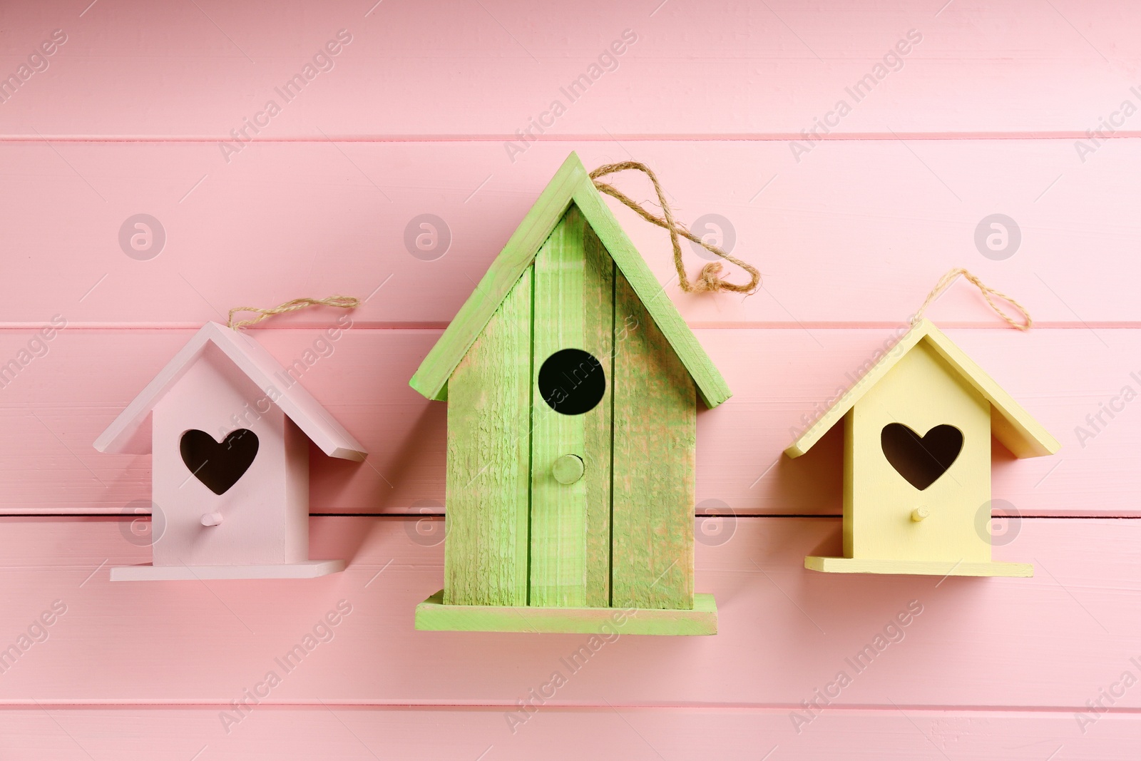 Photo of Three different bird houses on pink wooden background