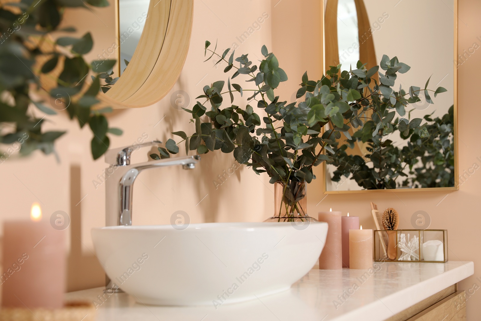 Photo of Eucalyptus branches near vessel sink on bathroom vanity. Interior design