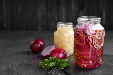 Photo of Jars of pickled onions on grey table. Space for text
