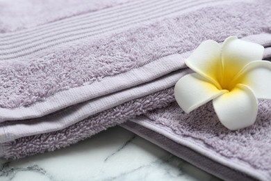 Photo of Violet terry towels and plumeria flower on white marble table, closeup