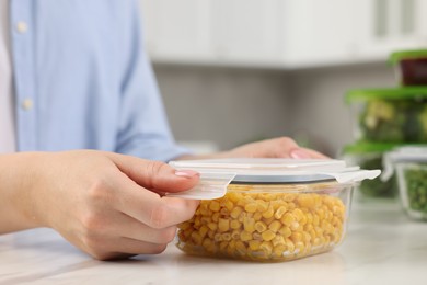 Photo of Woman sealing container with corn at white marble table in kitchen, closeup. Food storage