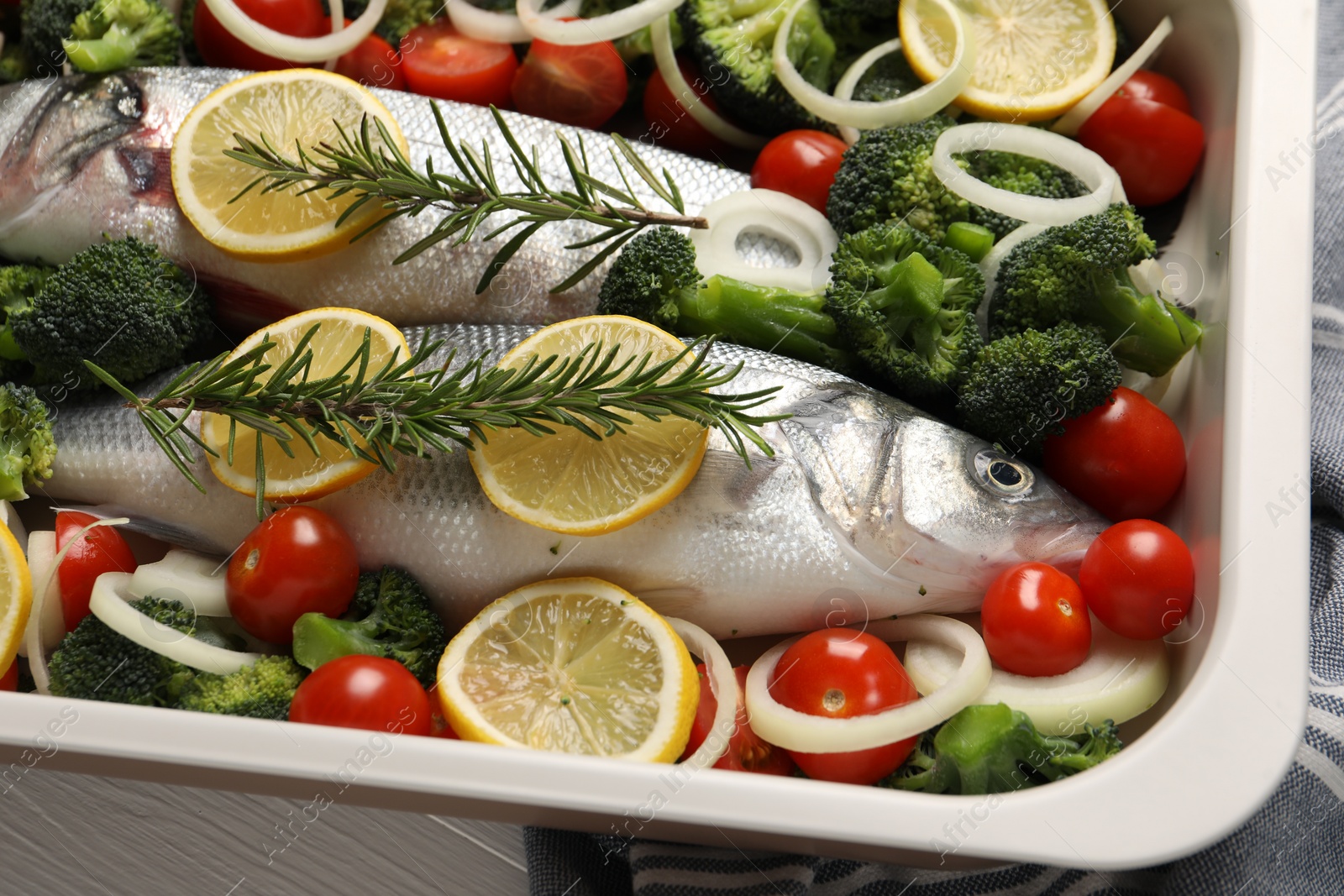 Photo of Raw fish with vegetables and lemon in baking dish on white table