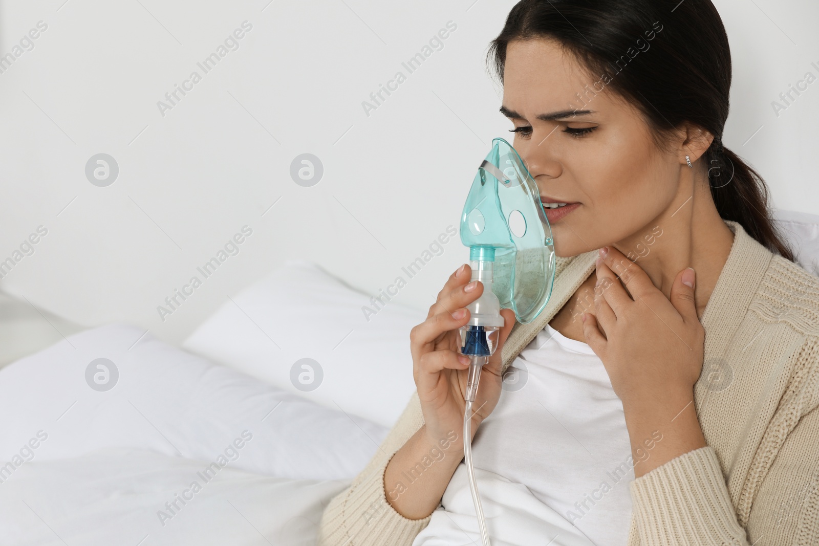 Photo of Sick young woman using nebulizer on bed at home, space for text