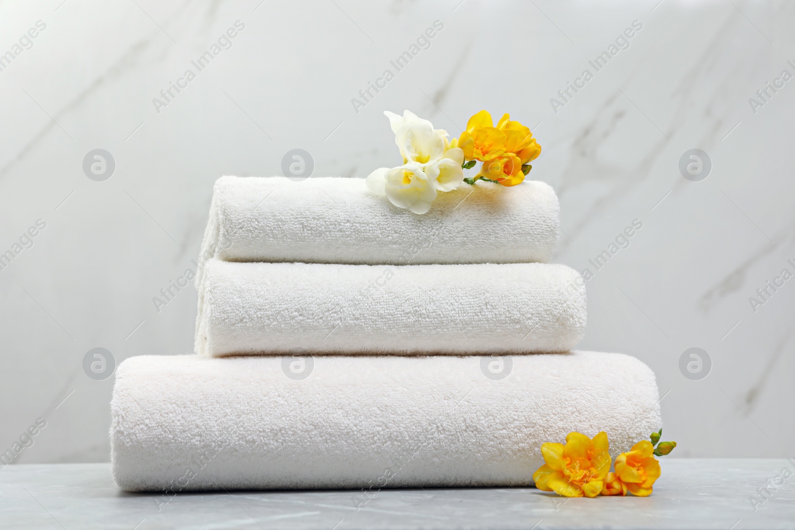 Photo of Stack of fresh towels with flowers on grey table against light background