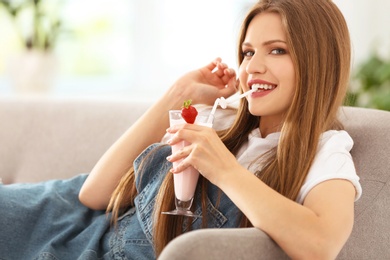 Young woman with glass of delicious milk shake indoors