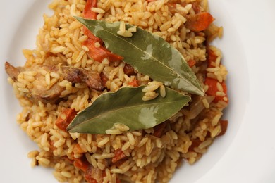 Photo of Delicious pilaf and bay leaves on plate, top view