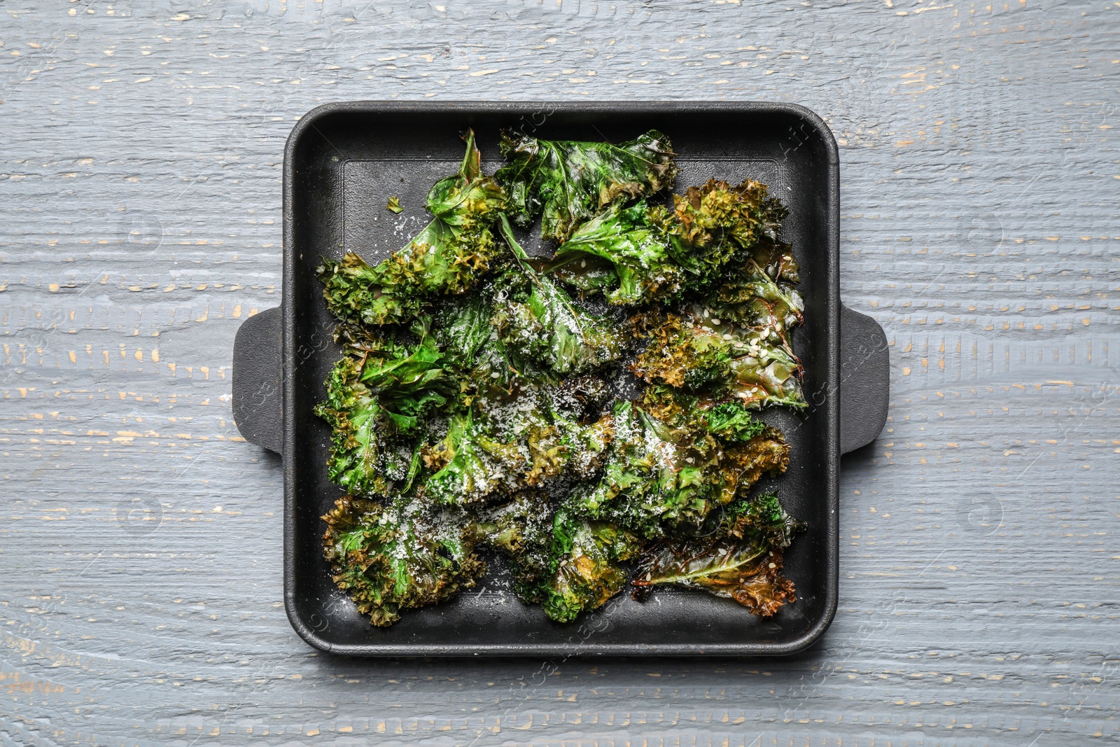 Photo of Tasty baked kale chips on light grey wooden table, top view