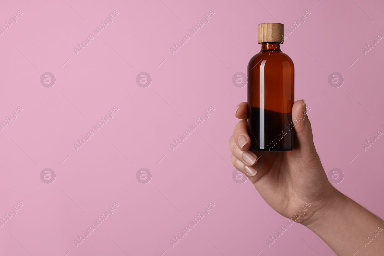 Photo of Woman holding bottle of cosmetic product on pink background, closeup. Space for text