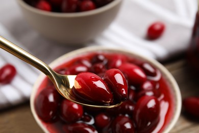 Photo of Spoon with delicious dogwood jam and berries over bowl, closeup