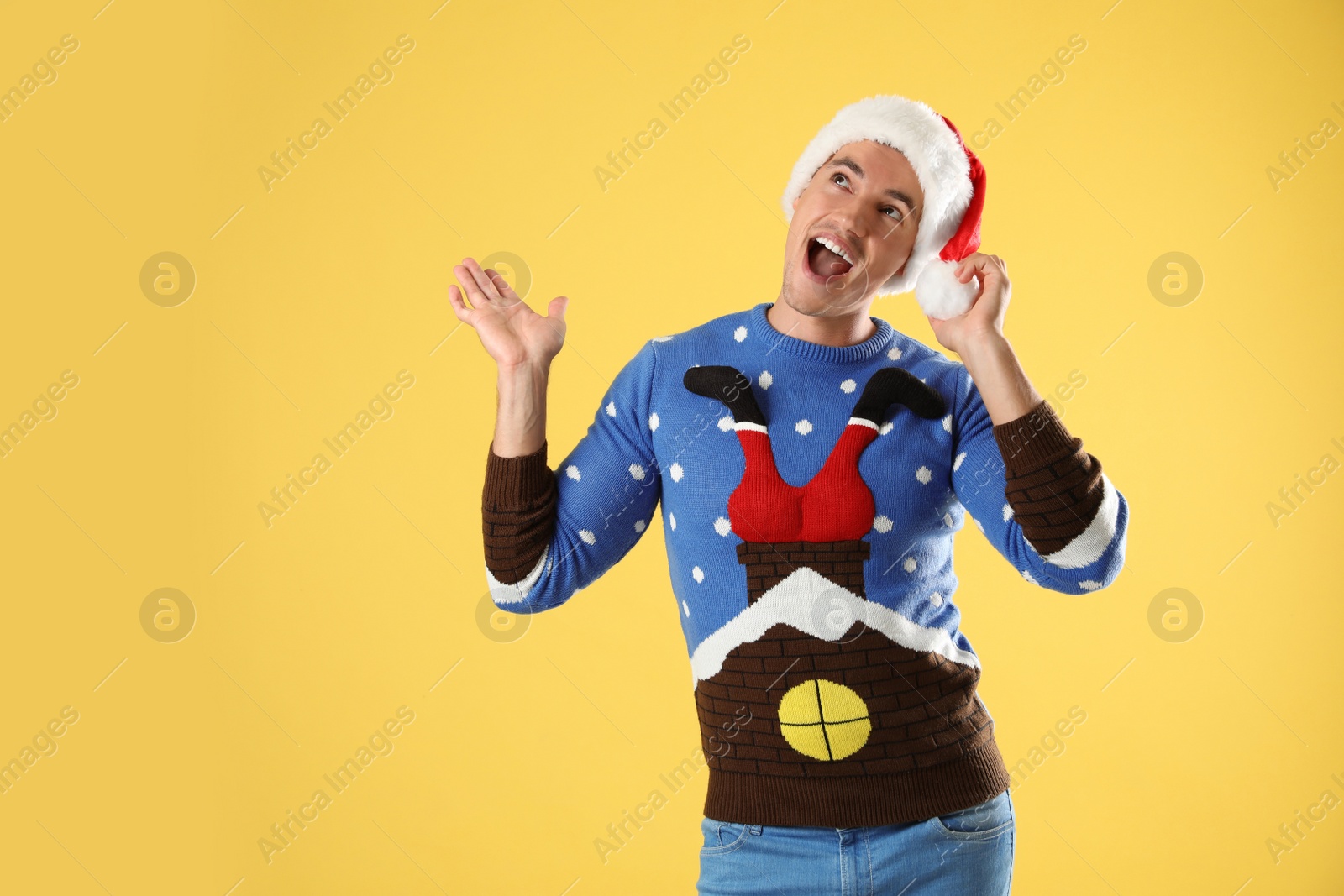 Photo of Portrait of young man in Christmas sweater and Santa hat on yellow background