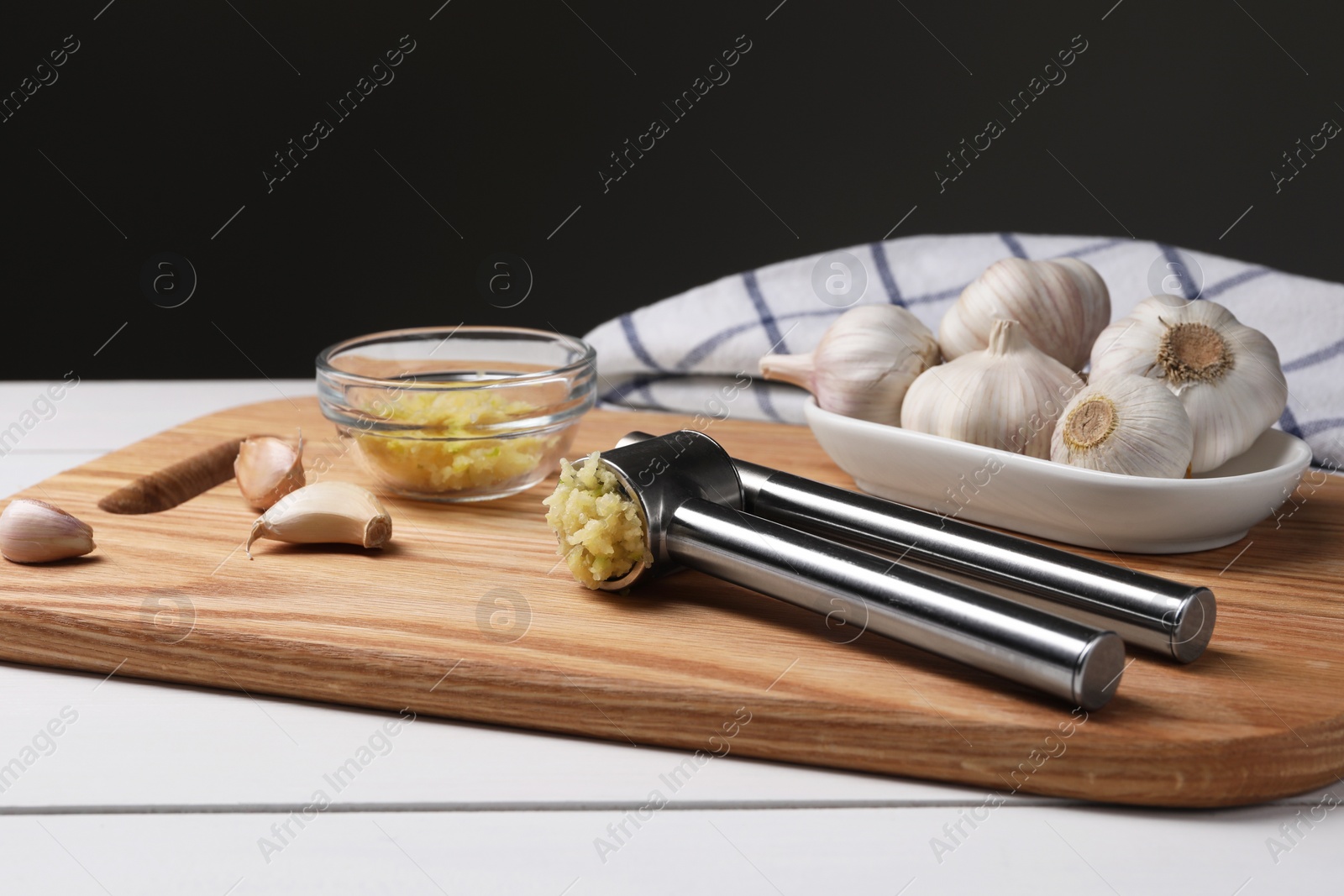 Photo of One metal press and garlic on white wooden table