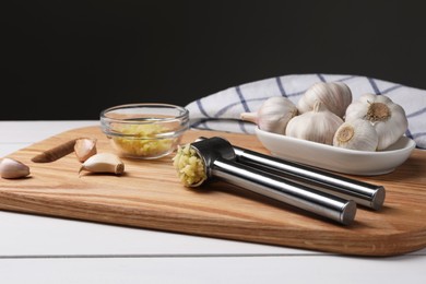 Photo of One metal press and garlic on white wooden table