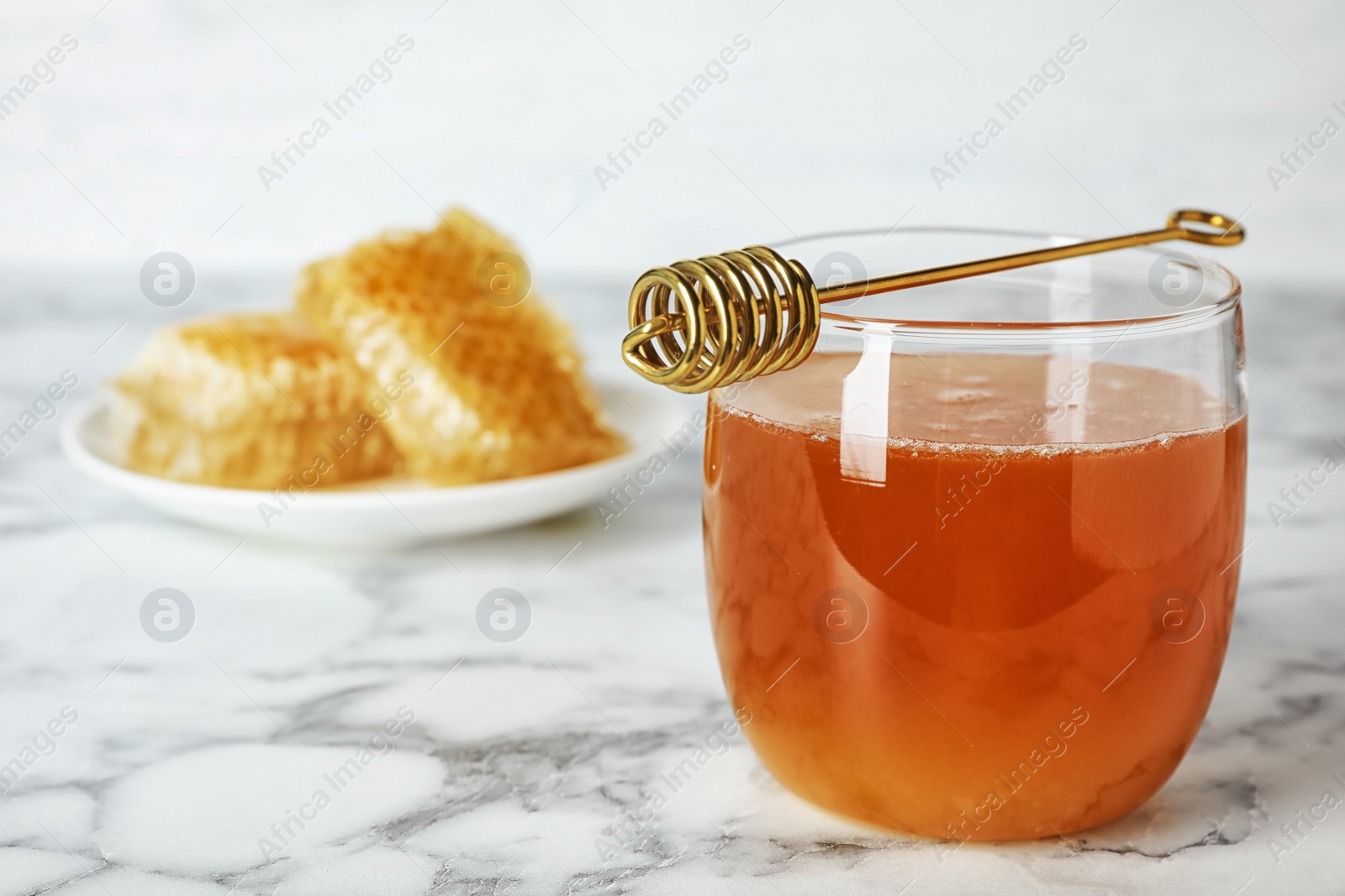 Photo of Glass with sweet honey and dipper on marble table