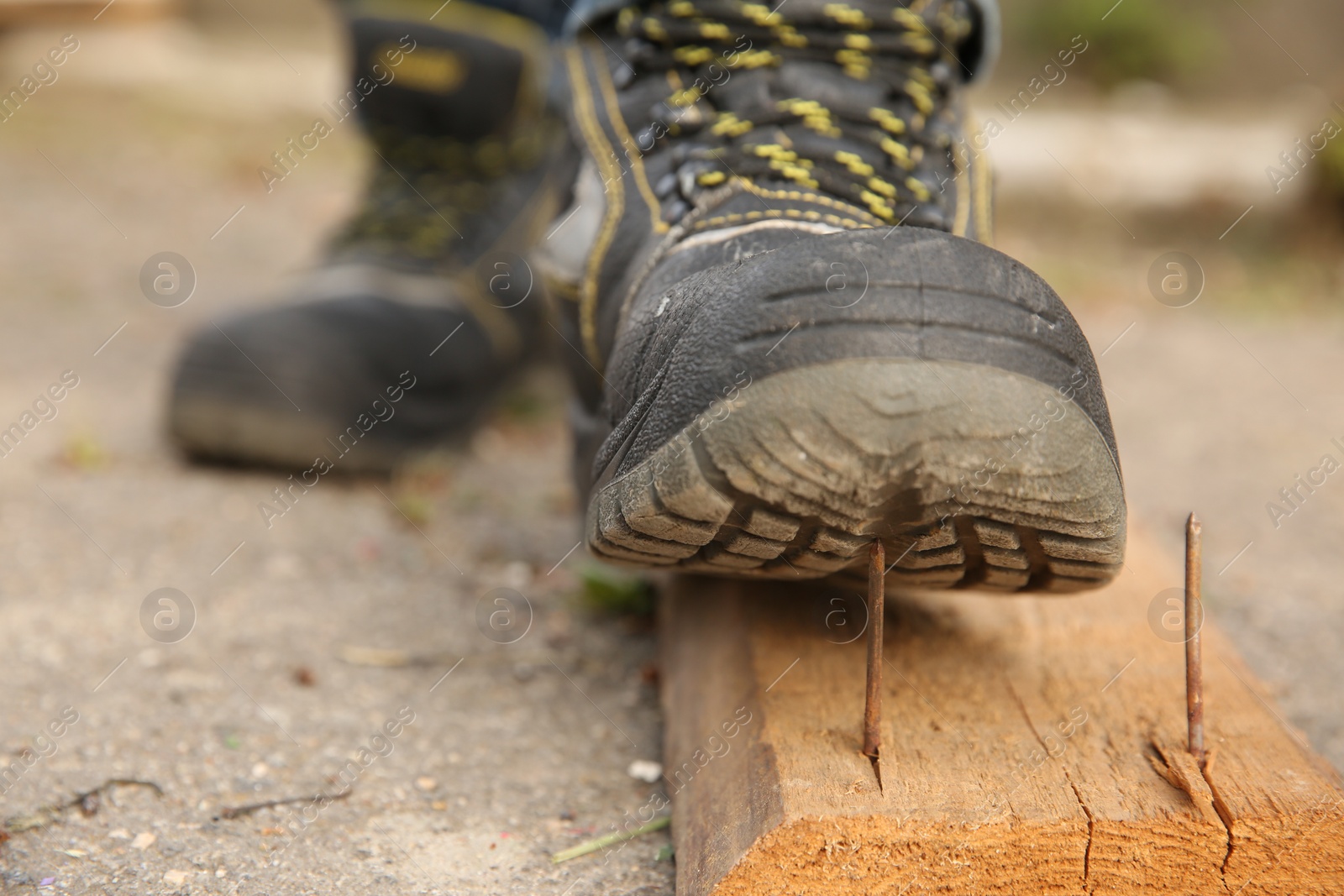 Photo of Careless worker stepping on nail in wooden plank outdoors, closeup