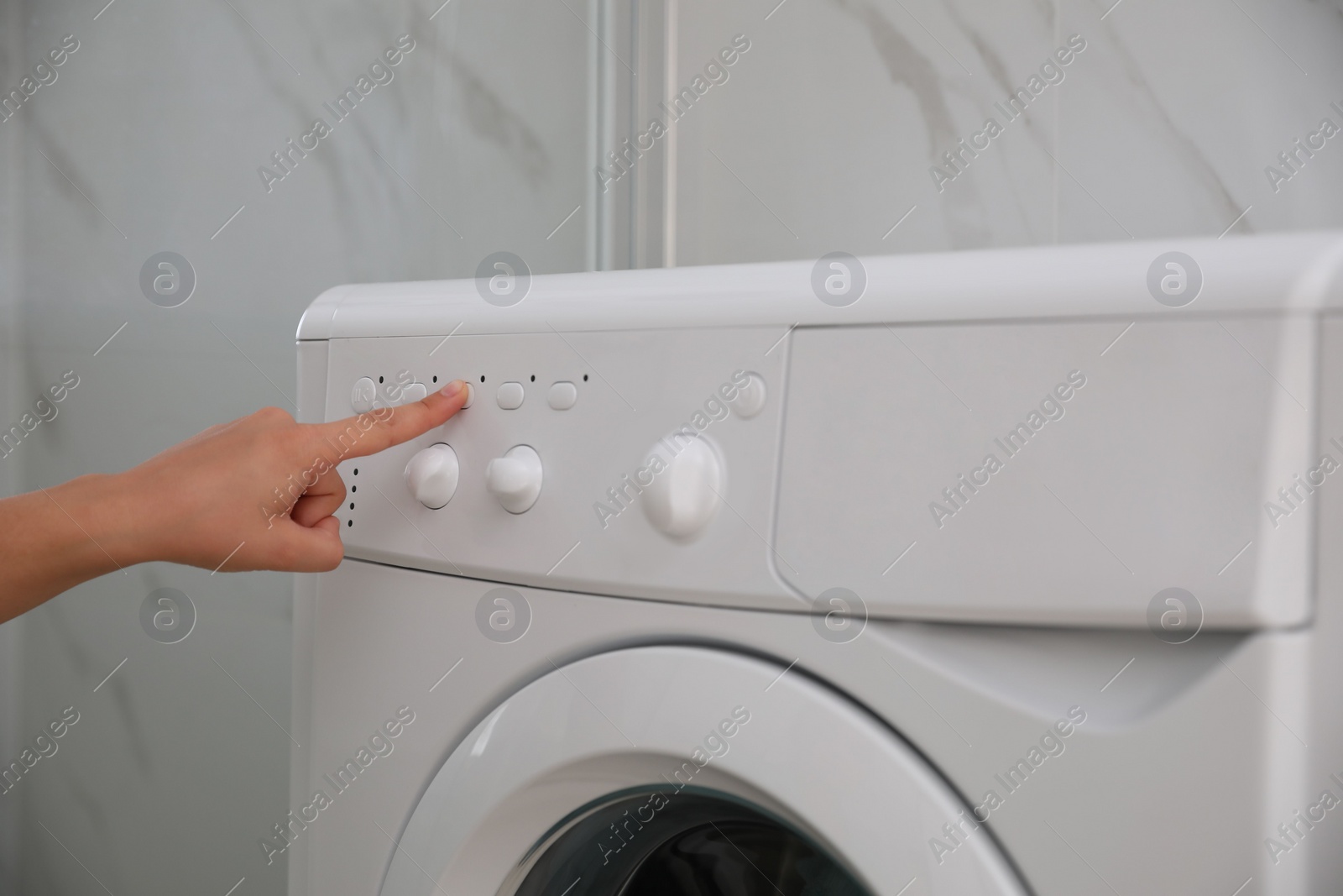 Photo of Woman pressing button on washing machine in bathroom, closeup