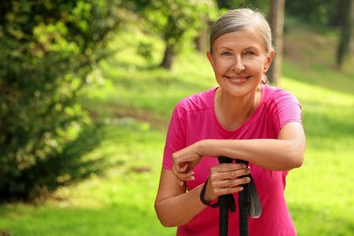 Photo of Senior woman with Nordic walking poles outdoors, space for text