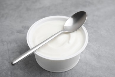 Photo of Delicious natural yogurt in plastic cup and spoon on grey table, closeup