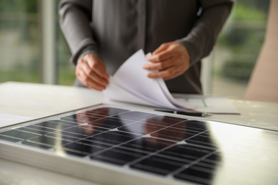 Photo of Solar panel and blurred person with papers on background, closeup