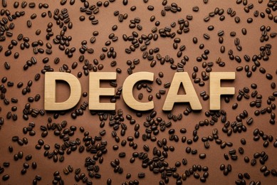 Photo of Word Decaf made of wooden letters on brown background with coffee beans, flat lay