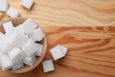 Photo of White sugar cubes in bowl on wooden table, top view. Space for text