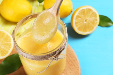 Photo of Taking delicious lemon curd from bowl at light blue wooden table, closeup