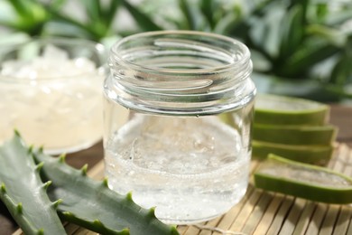 Photo of Aloe vera gel in jar and slices of plant on bamboo mat, closeup