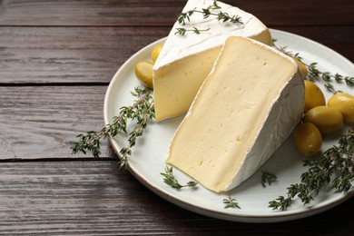 Photo of Plate with pieces of tasty camembert cheese, olives and rosemary on wooden table, closeup. Space for text