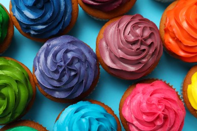 Many delicious colorful cupcakes on light blue background, flat lay