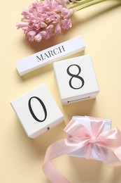 International Women's day - 8th of March. Gift box, wooden block calendar and beautiful flowers on beige background, flat lay