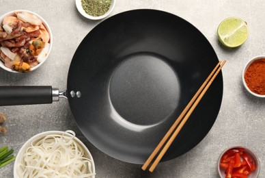 Flat lay composition with black wok, spices and products on grey textured table