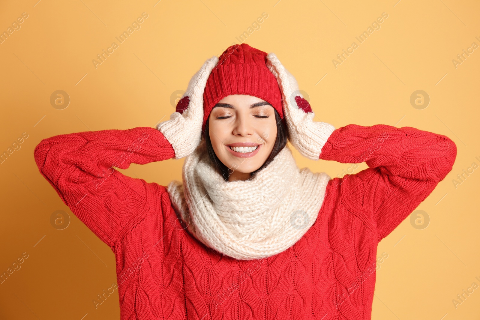 Photo of Young woman wearing warm sweater, scarf, mittens and hat on yellow background. Winter season