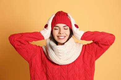 Photo of Young woman wearing warm sweater, scarf, mittens and hat on yellow background. Winter season