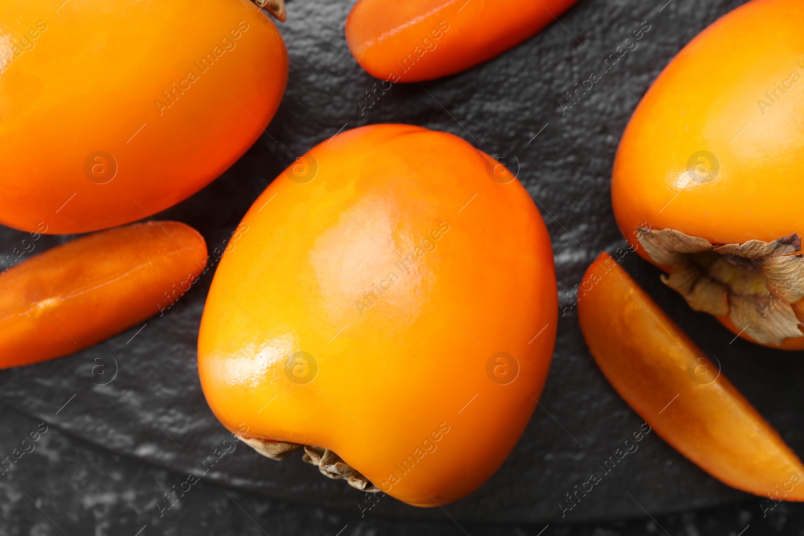 Photo of Delicious ripe persimmons on dark textured table, top view