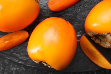 Photo of Delicious ripe persimmons on dark textured table, top view