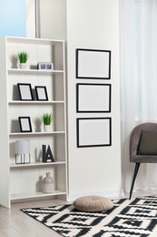 Photo of Stylish room interior with empty frames hanging on white wall near shelving unit