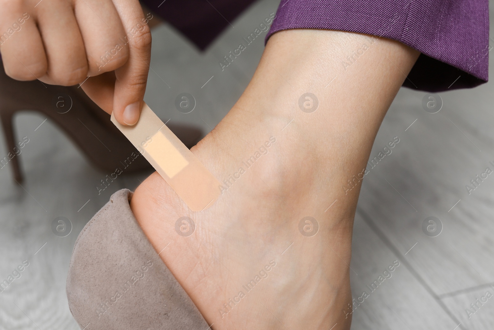 Photo of Female plastering her heel on wooden floor, closeup view