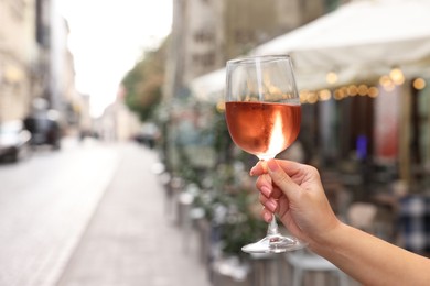 Woman holding glass of rose wine outdoors, closeup. Space for text