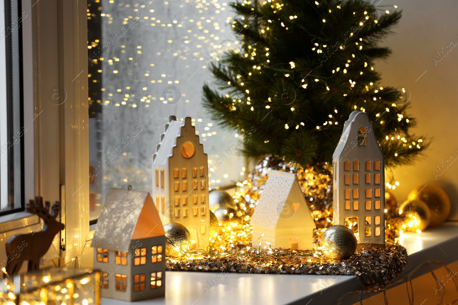 Photo of Beautiful decorative houses, baubles and small Christmas tree on window sill indoors