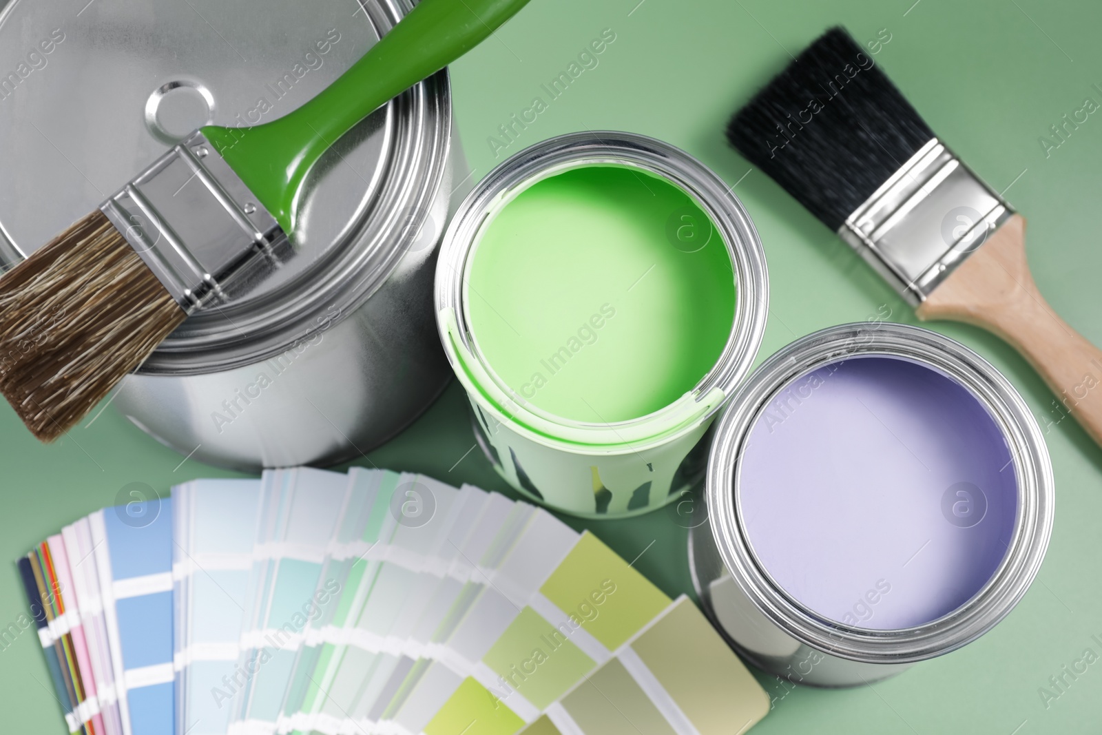 Photo of Cans of paints, palette and brushes on light green background, flat lay