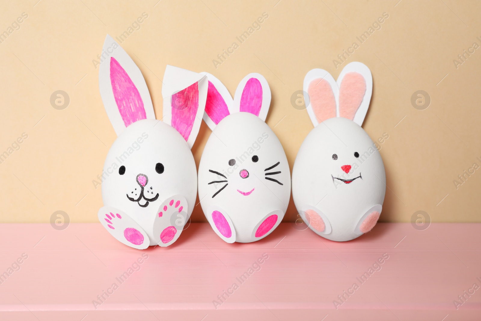 Photo of Eggs as cute bunnies on pink wooden table against beige background. Easter celebration