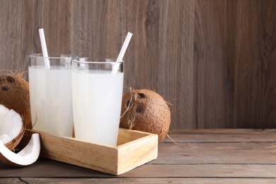 Glasses of coconut water with straws and nuts on wooden table, space for text