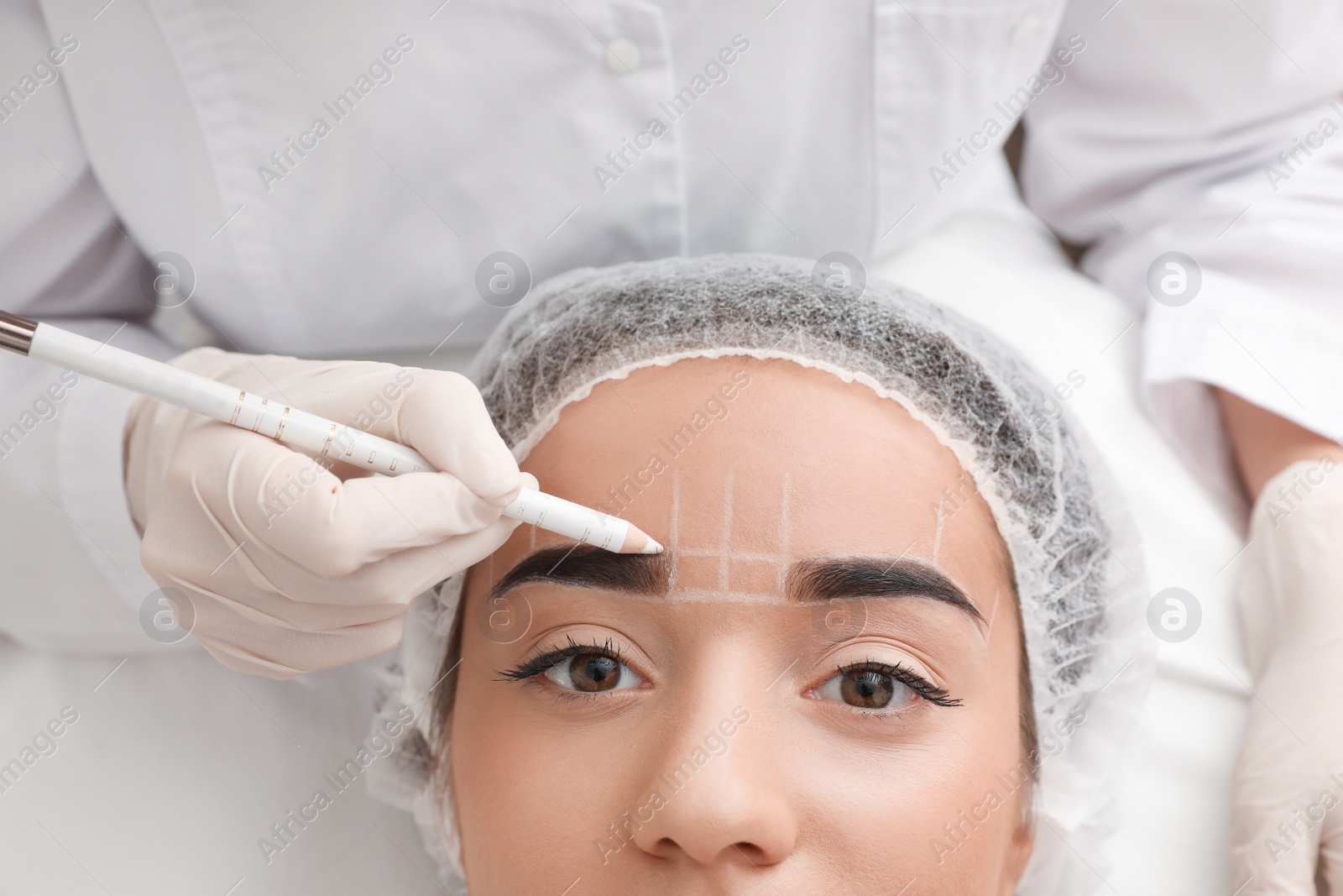 Photo of Young woman getting prepared for procedure of permanent eyebrow makeup in tattoo salon, closeup