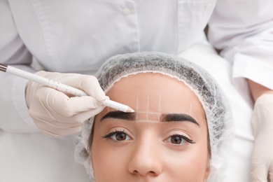 Photo of Young woman getting prepared for procedure of permanent eyebrow makeup in tattoo salon, closeup