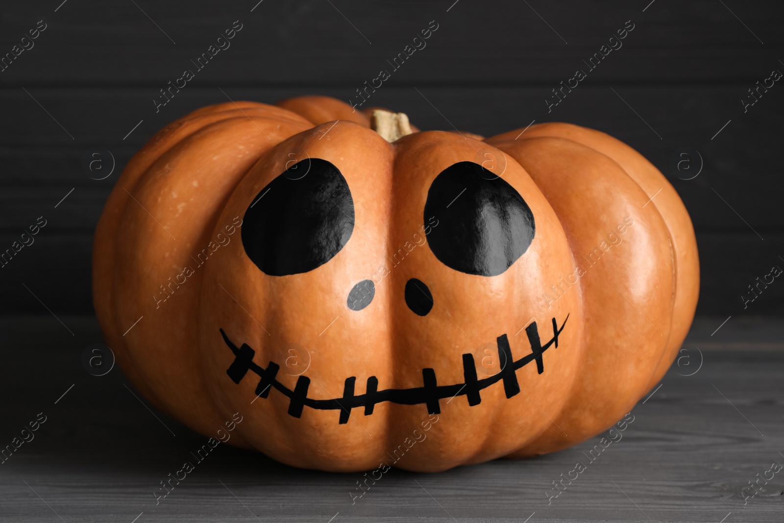 Photo of Pumpkin with drawn spooky face on grey table. Halloween celebration