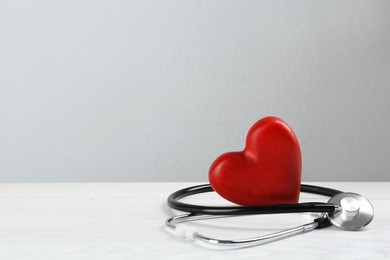 Photo of Stethoscope and red heart on white wooden table, space for text. Cardiology concept