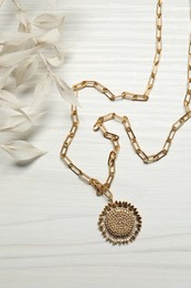 Elegant necklace and dry leaves on white wooden table, top view