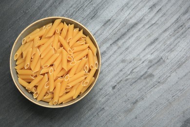 Raw penne pasta in bowl on grey table, top view