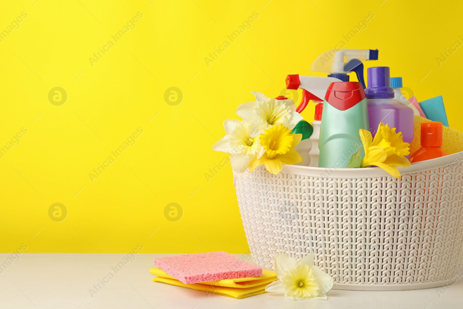 Photo of Plastic basket with spring flowers and cleaning supplies on wooden table. Space for text