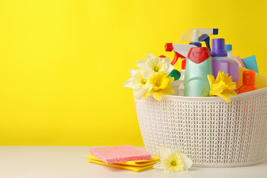 Photo of Plastic basket with spring flowers and cleaning supplies on wooden table. Space for text